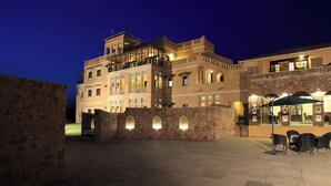 A historic building with multiple balconies and arched windows, a courtyard with stone walls, and outdoor seating.
