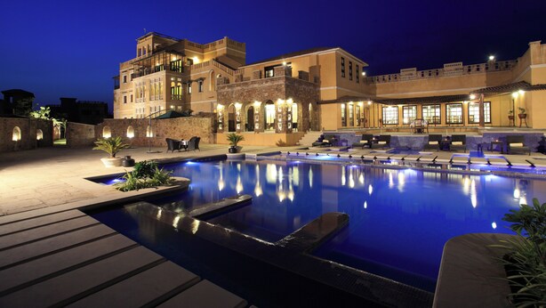 A hotel with a swimming pool, outdoor seating, and a well-lit facade.