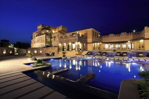 A hotel with a swimming pool, outdoor seating, and a well-lit facade. - Juna Mahal Jungle Resort (Sawai Madhopur)