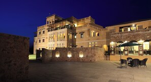 A historic building with multiple balconies and arched windows, a courtyard with stone walls, and outdoor seating.