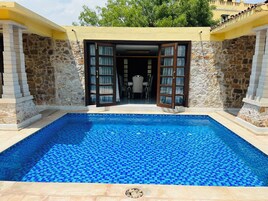 Una piscina con suelo de baldosas, paredes de piedra y una puerta que da a un espacio interior.