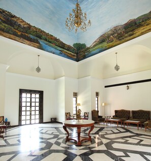 A spacious room with a large chandelier, a round table, and a seating area with sofas. - Juna Mahal Jungle Resort (Sawai Madhopur)