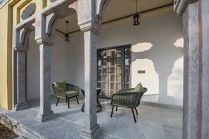 A covered outdoor seating area with chairs and a table, a window with a view, and a door. - Juna Mahal Jungle Resort (Sawai Madhopur)