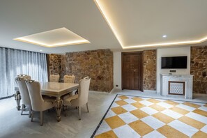 A dining area with a table and chairs, a stone wall, a fireplace, and a television mounted above it.