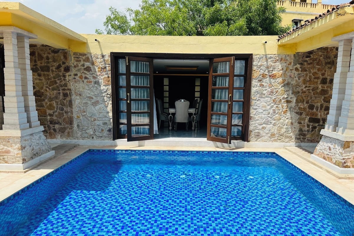 A swimming pool with a tiled floor, stone walls, and a door leading to an interior space.
