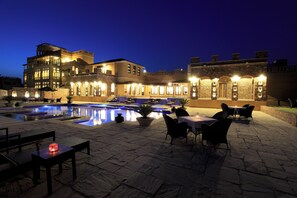 A poolside area with outdoor seating and a building with multiple levels and arched windows. - Juna Mahal Jungle Resort (Sawai Madhopur)