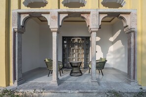 A covered outdoor area with a central table and two chairs, a door with glass panels, and a yellow wall. - Juna Mahal Jungle Resort (Sawai Madhopur)