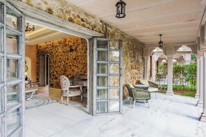 A stone-walled room with a dining area, a large window, and a view of a garden. - Juna Mahal Jungle Resort (Sawai Madhopur)