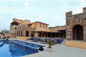 A hotel with a swimming pool, outdoor seating, and a stone facade.