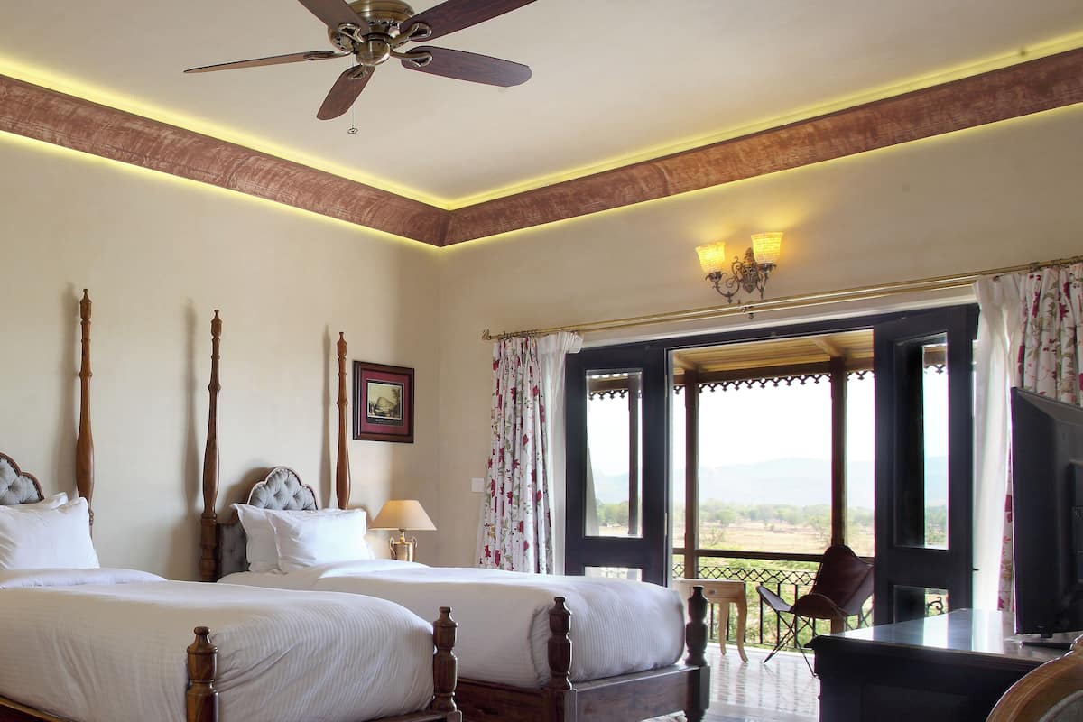 A bedroom with two beds, a ceiling fan, a desk with a chair, and a view through an open door.