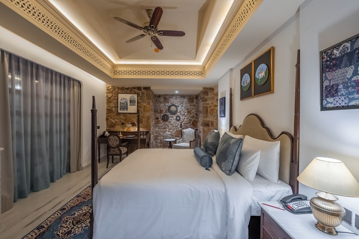 A hotel room with a bed, a desk, a chair, a stone wall, and a ceiling fan.