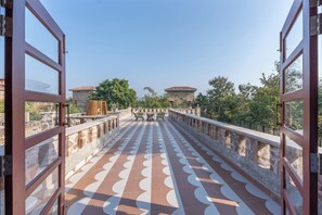 A terrace with a patterned floor, stone walls, and a view of a building with a red roof.
