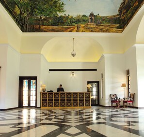 A lobby with a reception desk, a chandelier, and a mural on the ceiling.