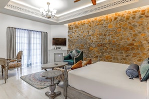 A hotel room with a stone accent wall, a bed, a round coffee table, a sofa, and a chandelier. - Juna Mahal Jungle Resort (Sawai Madhopur)