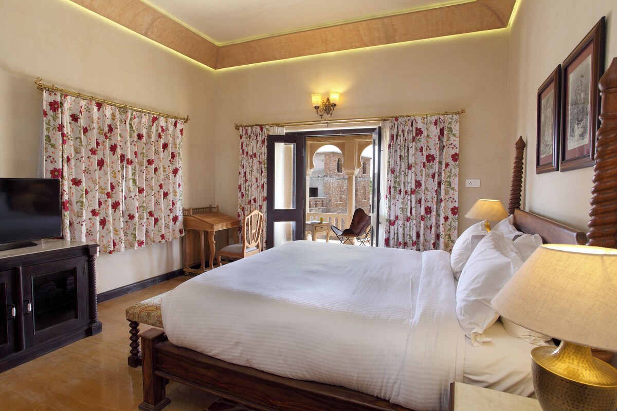 A hotel room with a large bed, a desk, a chair, a television, and a lamp.