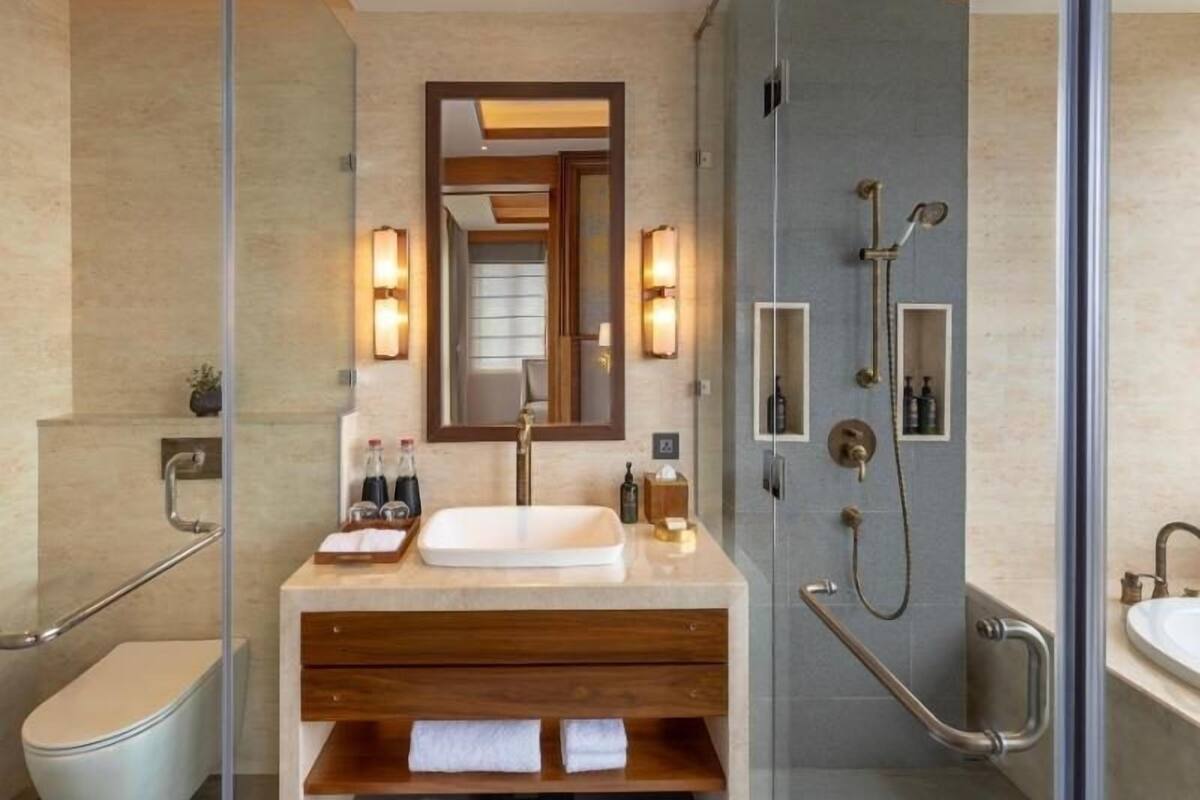 Un baño moderno con ducha envuelta en cristal, tocador de madera, espejo grande y un inodoro.