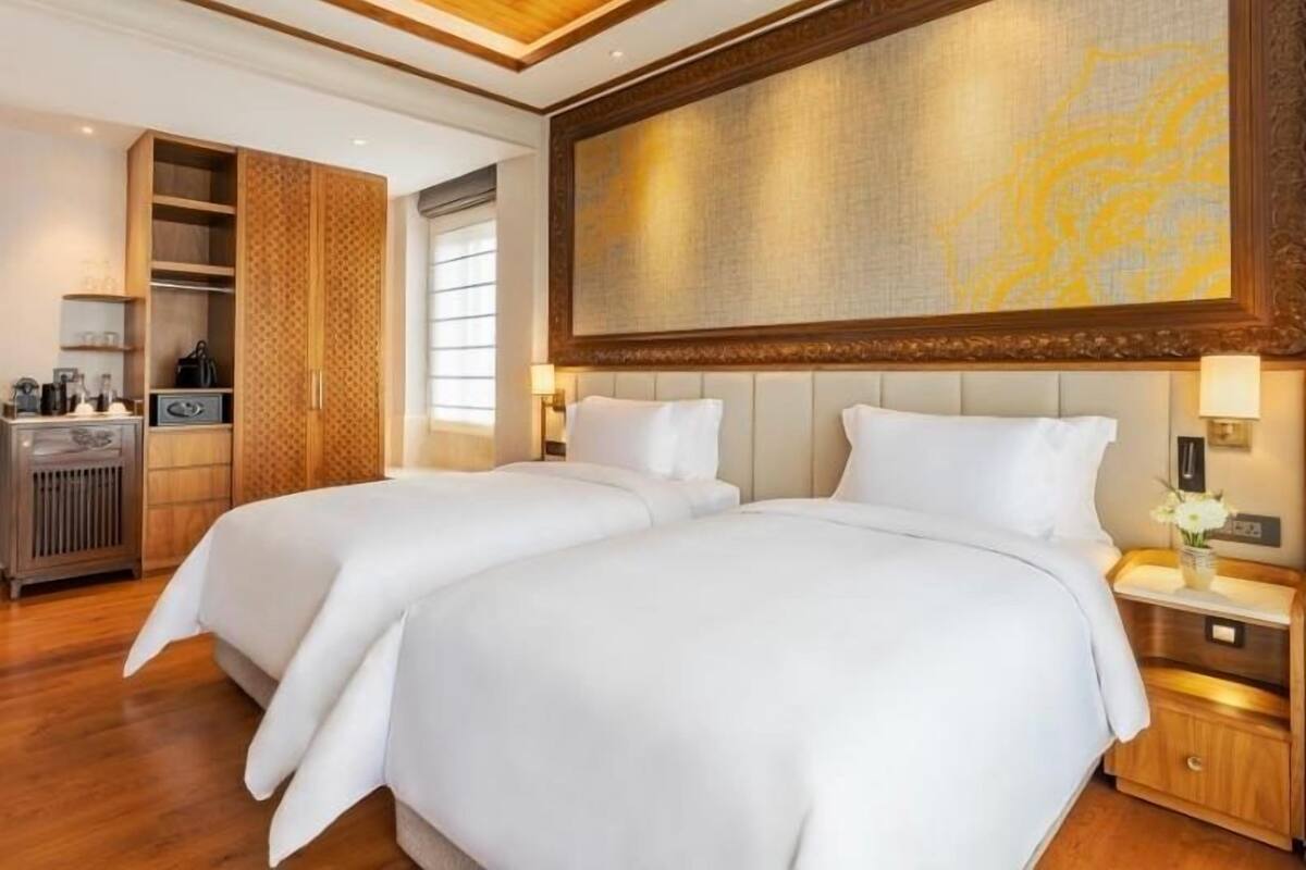 Habitación de hotel con dos camas, techo de madera, un cuadro abstracto grande y un armario.