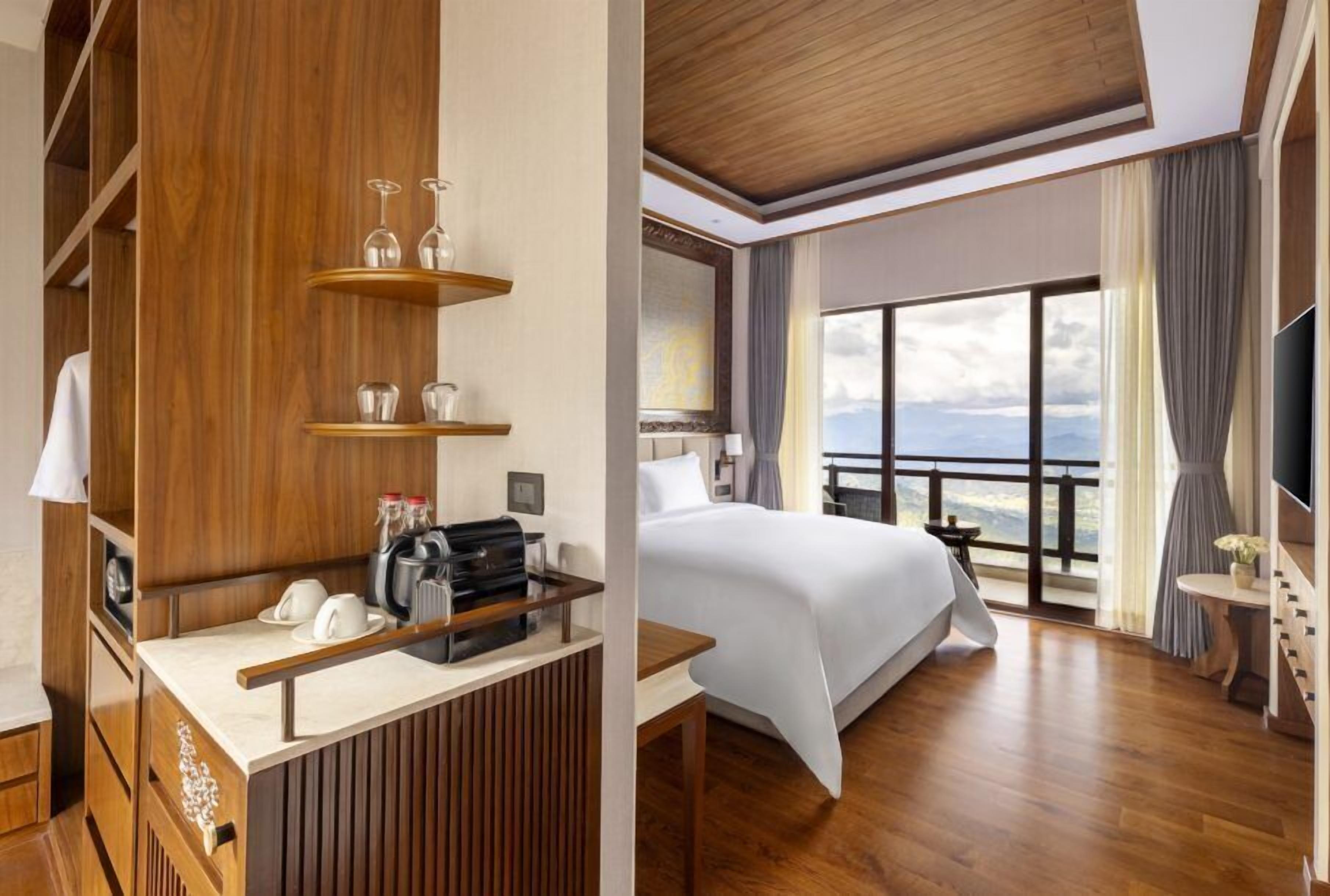 A hotel room with a bed, a desk with a telephone, a TV, and a large window with a view.
