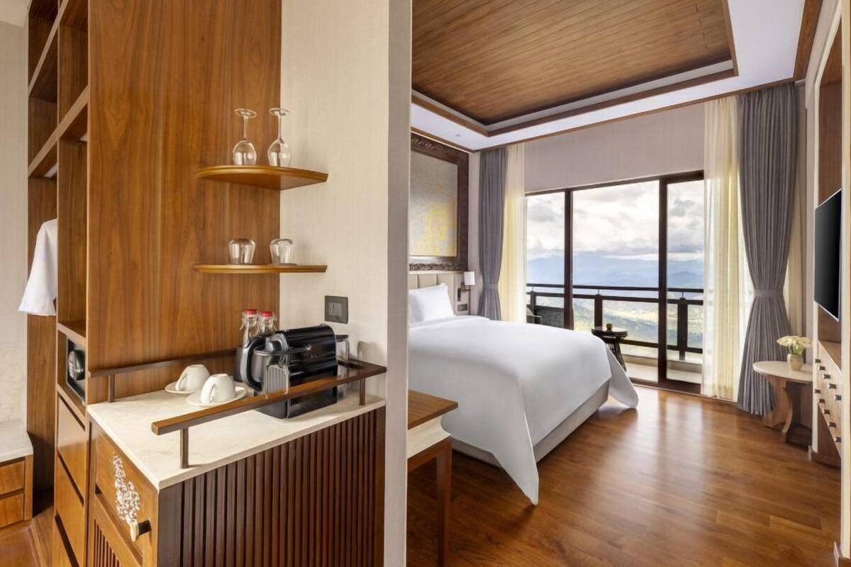 Una habitación de hotel con cama, escritorio, teléfono, televisión y un gran ventanal con vistas.