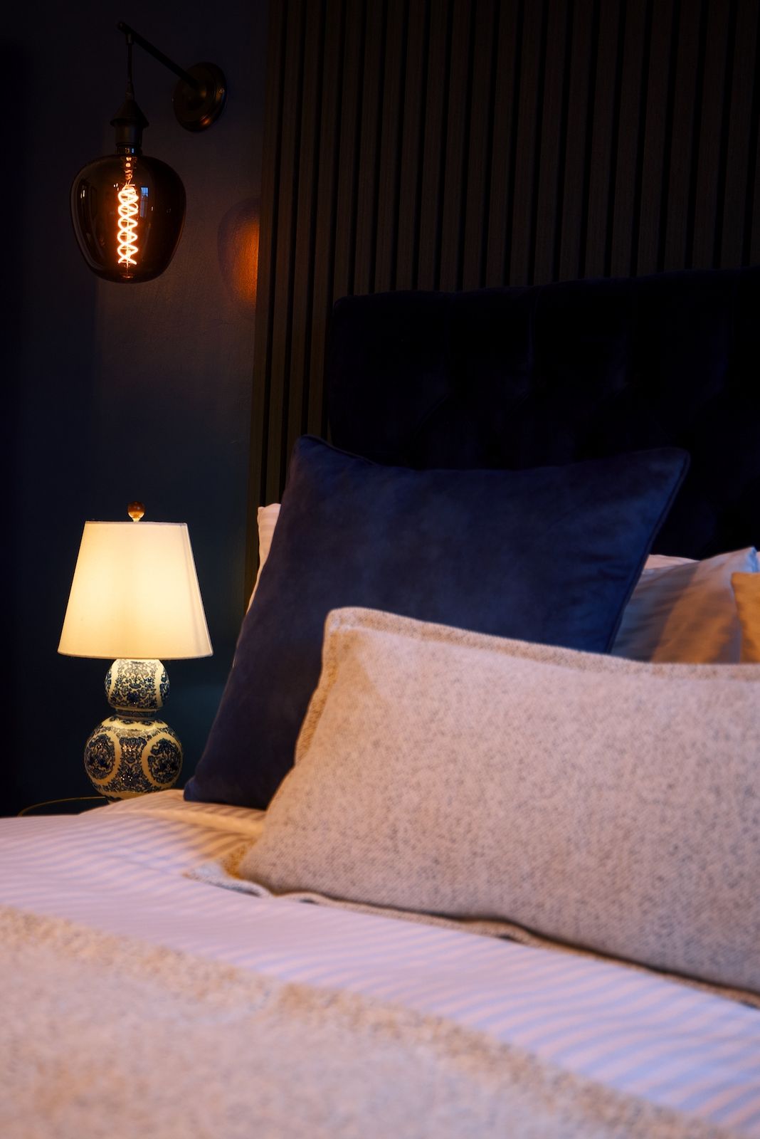 A bed with pillows, a lamp, and a wall-mounted light fixture.