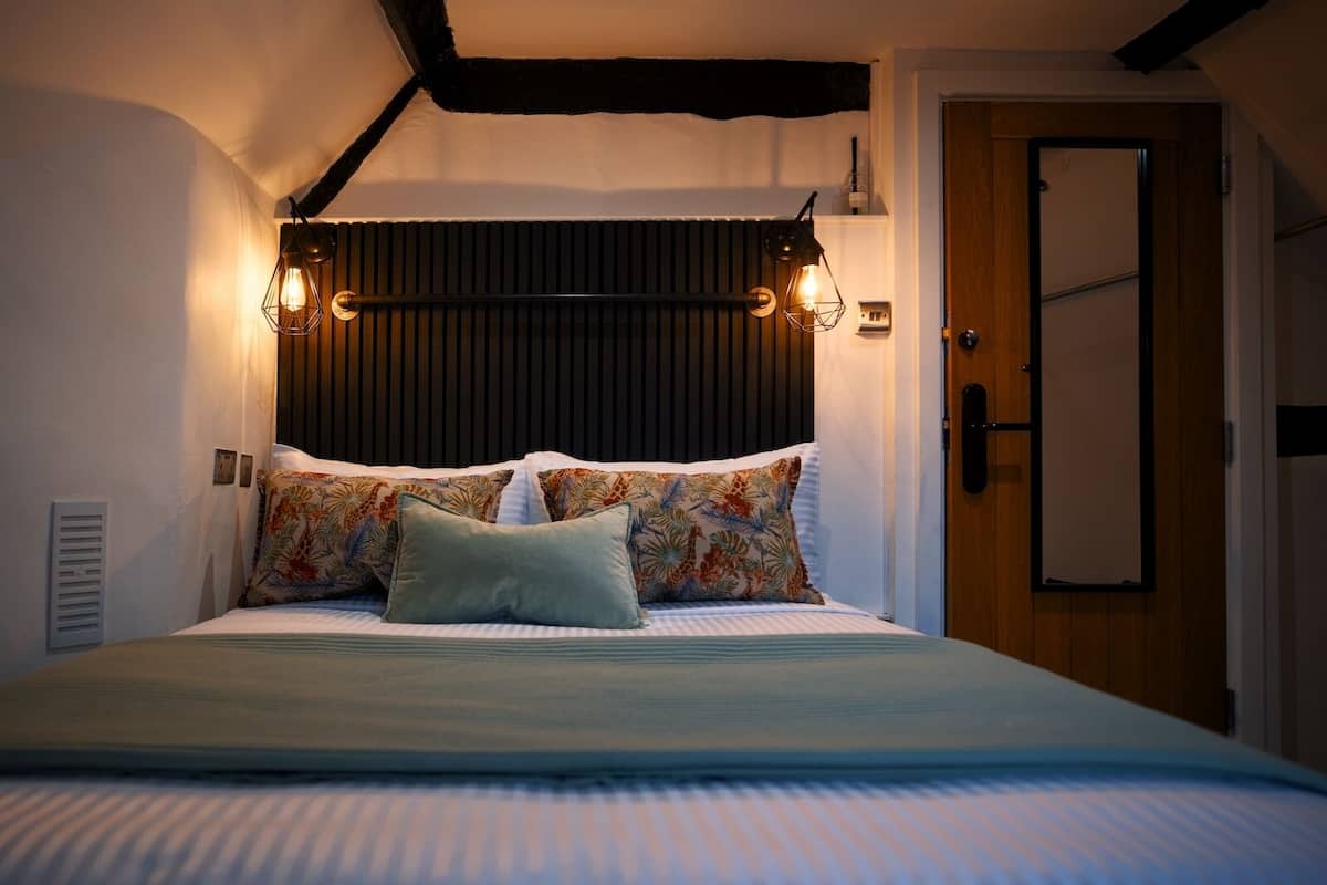 A bedroom with a bed, pillows, a headboard, wall-mounted lights, a door, and a vent.