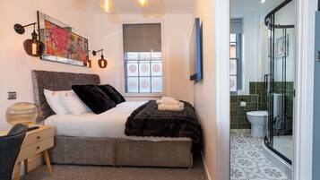 A bedroom with a bed, bedside table, lamp, artwork, and a window.