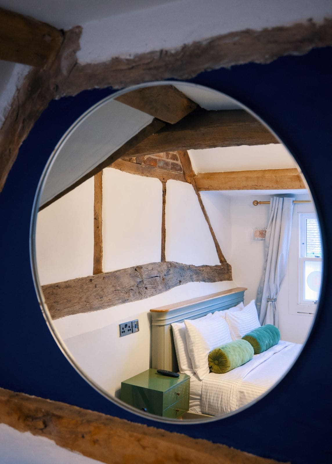 A bedroom with exposed wooden beams, a bed with pillows, a nightstand, and a window with curtains.