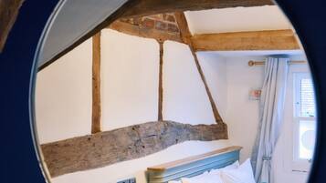 A bedroom with exposed wooden beams, a bed with pillows, a nightstand, and a window with curtains.