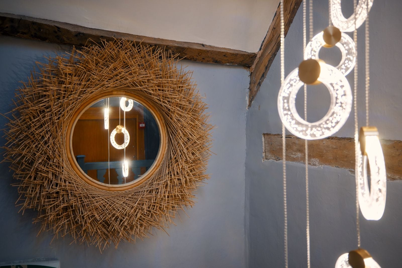 A circular mirror with a straw-like border, a wooden beam, and hanging light fixtures.