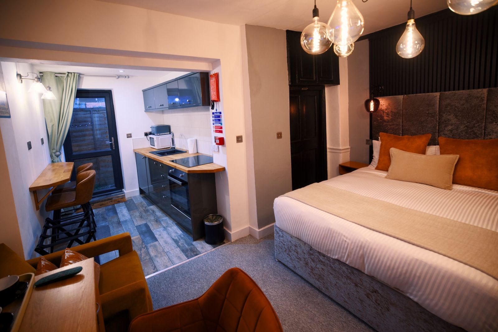 Habitación de hotel pequeña con cama, una kitchenette, zona de comedor y vistas a través de una puerta.