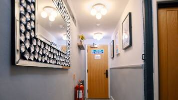 A hallway with patterned floor tiles, a fire extinguisher, a mirror with a diamond pattern, and a door at the end.