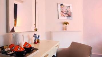 A hotel room with a large mirror, a desk with Yorkshire Tea packets, a chair, a framed picture on the wall, and a small vase with flowers.