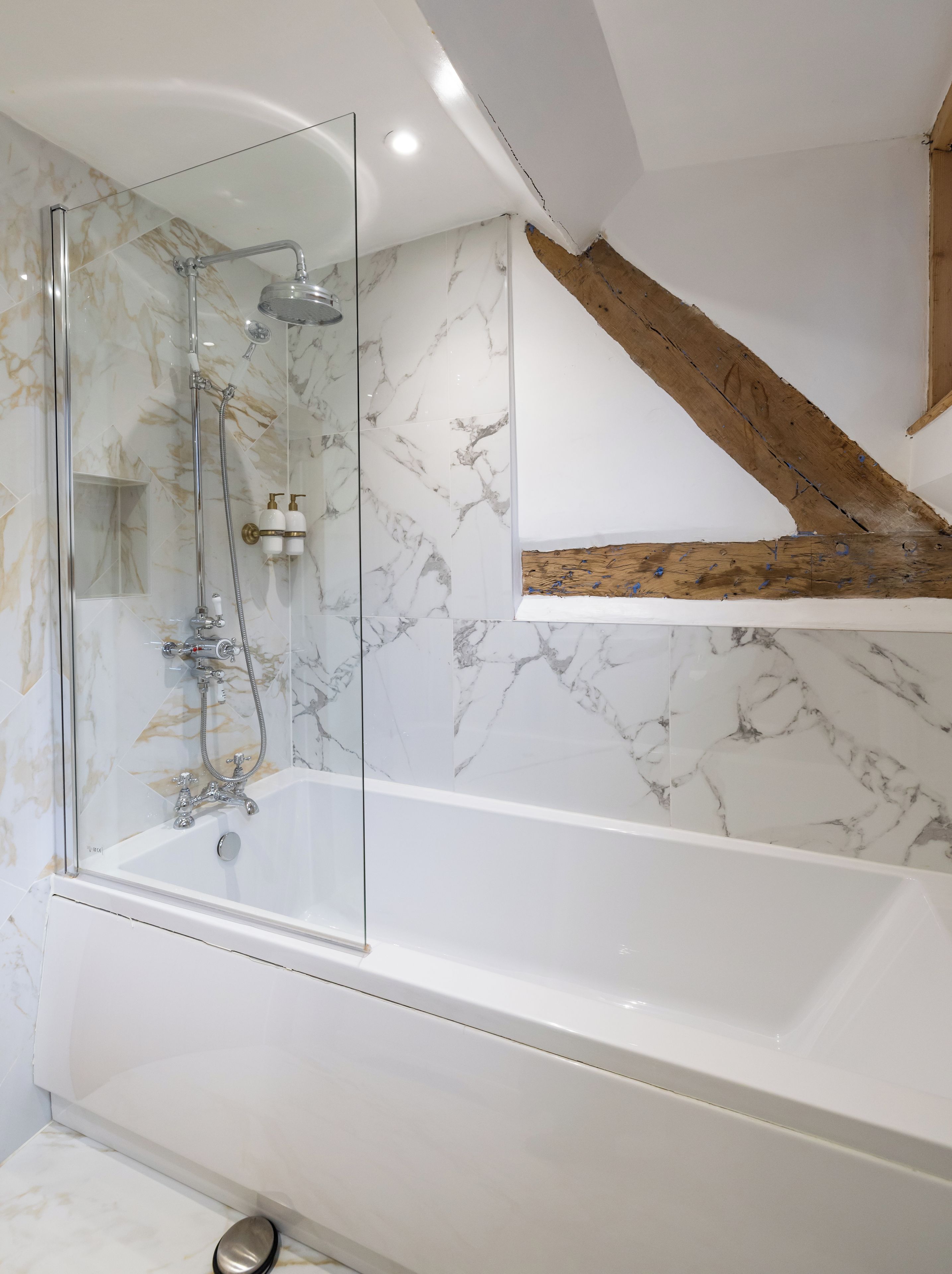 A modern bathroom with a glass-enclosed shower, a white bathtub, marble walls, and a wooden beam structure.