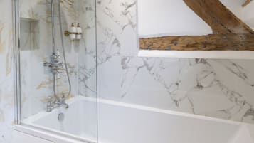 Une salle de bain moderne avec une douche à parois de verre, une baignoire blanche, des murs en marbre et une structure en poutres apparentes.