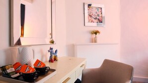 A hotel room with a large mirror, a desk with Yorkshire Tea packets, a chair, a framed picture on the wall, and a small vase with flowers. - City Rooms by Hiive (Worcester)