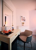 Habitación de hotel con un espejo grande, un escritorio con paquetes de té Yorkshire, una silla, un cuadro en la pared y un pequeño jarrón con flores.