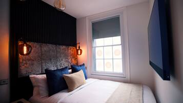 Une chambre à coucher comprenant un lit, des oreillers, une table de chevet, un téléviseur fixé au mur et deux luminaires suspendus.