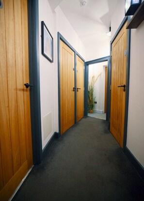 A hallway with wooden doors, a framed picture on the wall, and a potted plant. - City Rooms by Hiive (Worcester)