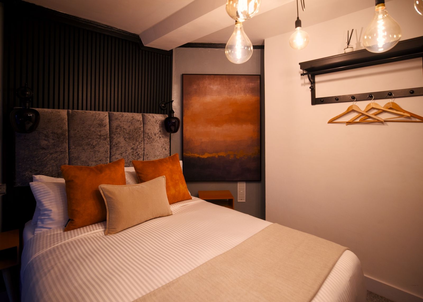 A modern bedroom with a large bed, a headboard with vertical slats, a wall-mounted light fixture, and a painting.