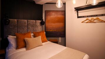 A modern bedroom with a large bed, a headboard with vertical slats, a wall-mounted light fixture, and a painting.