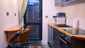 A compact kitchen with a dining area, a microwave, and a view through a glass door. - City Rooms by Hiive (Worcester)