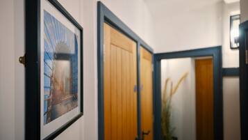 A hallway with framed artwork, wooden doors, and a plant.