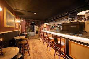 Una zona de bar con taburetes de madera, una barra con una máquina de café y una pared decorada con cuadros.