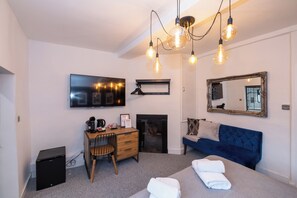 A modern bedroom with a bed, a desk, a chair, a TV, a fireplace, and a mirror. - City Rooms by Hiive (Worcester)