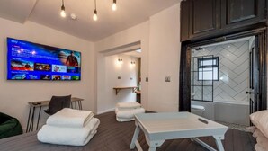 A modern hotel room with a bed, a massage table, a TV, and a bathroom with a bathtub. - City Rooms by Hiive (Worcester)