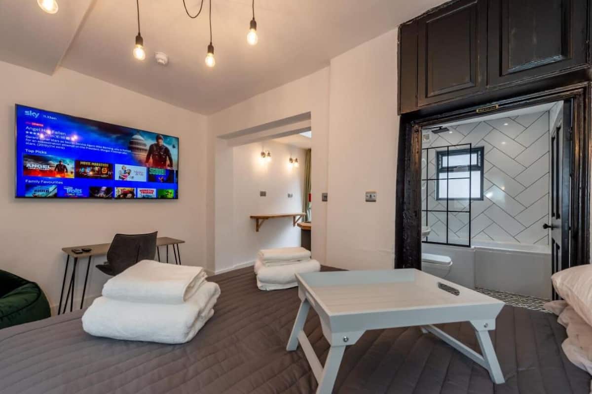 A modern hotel room with a bed, a massage table, a TV, and a bathroom with a bathtub.
