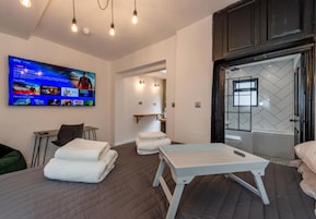 Una habitación de hotel moderna con cama, mesa de masaje, televisor y baño con bañera.