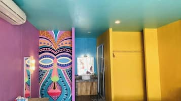 Une pièce décorée d’une fresque colorée, avec un lavabo et un banc en bois.
