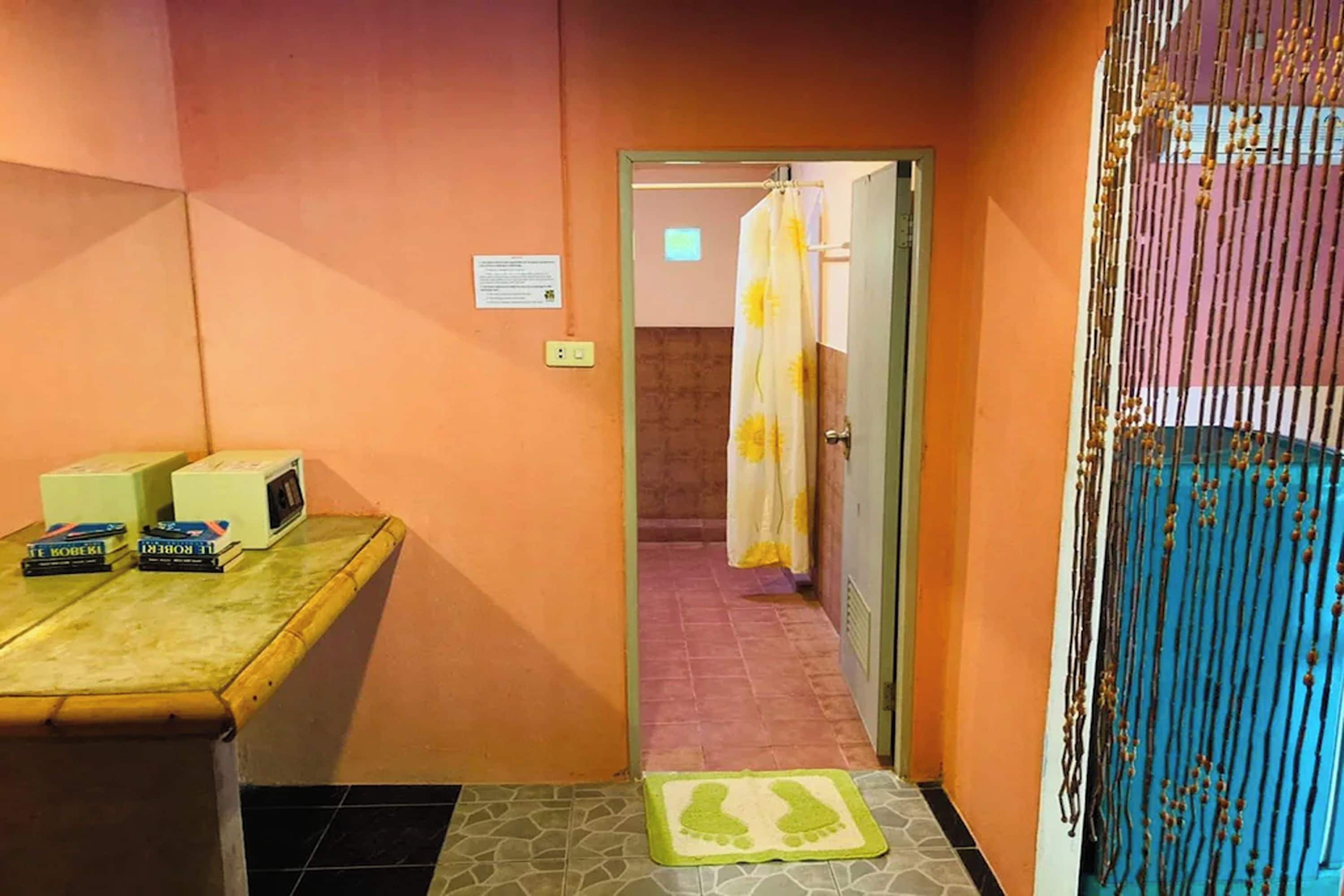 Un baño con cortina de ducha, una mesita con libros y un microondas, y un tapete en el suelo.