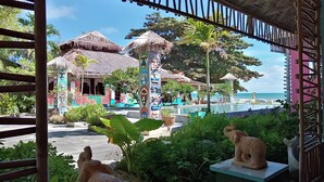 Un resort con edificios de techo de paja, piscina y vegetación tropical.